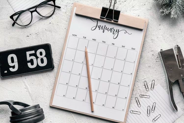 Table avec différents éléments : calendrier, horloge, lunettes, casque audio, agrafeuse, trombones, papier, crayon