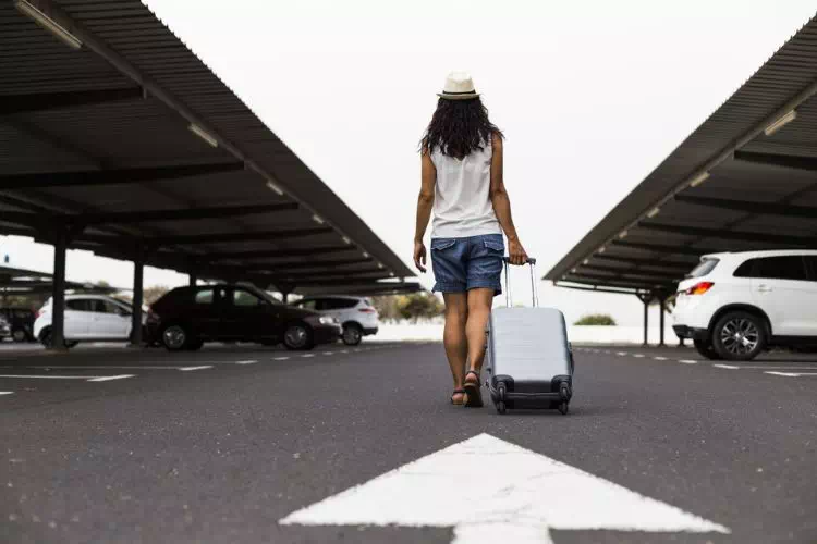 Femme marchant avec sa valise dans une des allées d'un parking d'aéroport