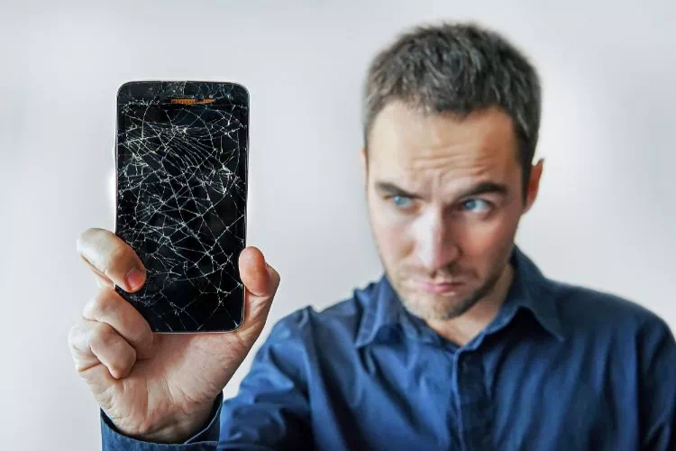 Homme attristé tenant un iPhone dont l'écran est totalement fissuré
