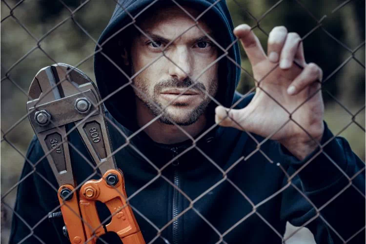 Voleur avec une pince monseigneur prêt à découper un grillage et entrer sur un chantier
