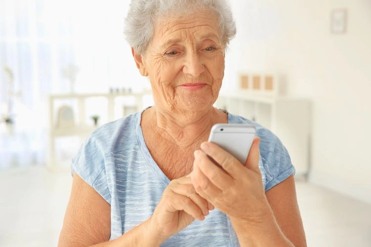 Femme âgée heureuse utilisant son smartphone pour les factures numériques après avoir reçu une aide