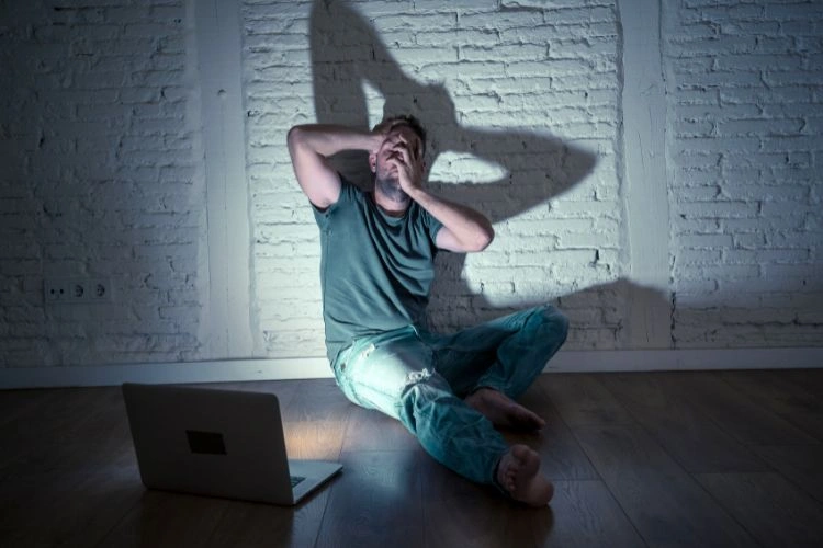 Homme dans une obscurité et cachant son visage face à un ordinateur représentant les différents types de revenge porn