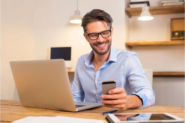 Homme heureux devant son ordinateur et son téléphone ne faisant pas attention aux mauvais commentaires sur les réseaux sociaux