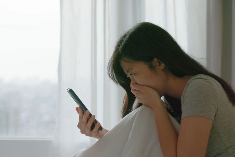 Jeune femme sur son lit avec son téléphone en main victime de sextorsion