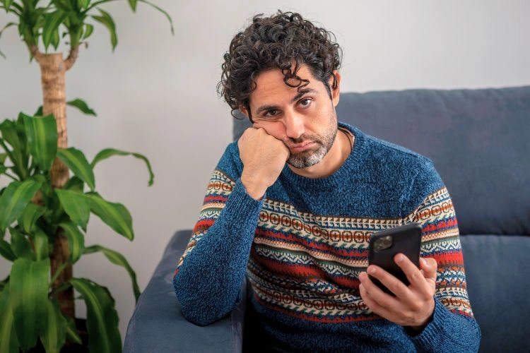 Homme victime de sextorsion en pleine dépression avec son téléphone dans la main
