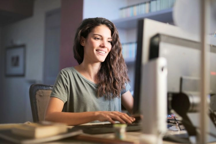 Femme heureuse devant son ordinateur parce qu'elle évite le cyberharcèlement